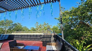 Un área de estar al aire libre cubierta con sillones reclinables y una mesa, rodeada de árboles y un cielo despejado.