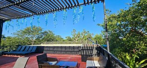 A covered outdoor seating area with lounge chairs and a table, surrounded by trees and a clear sky. - Cuatro Elementos Noh By GEstores (Tulum)