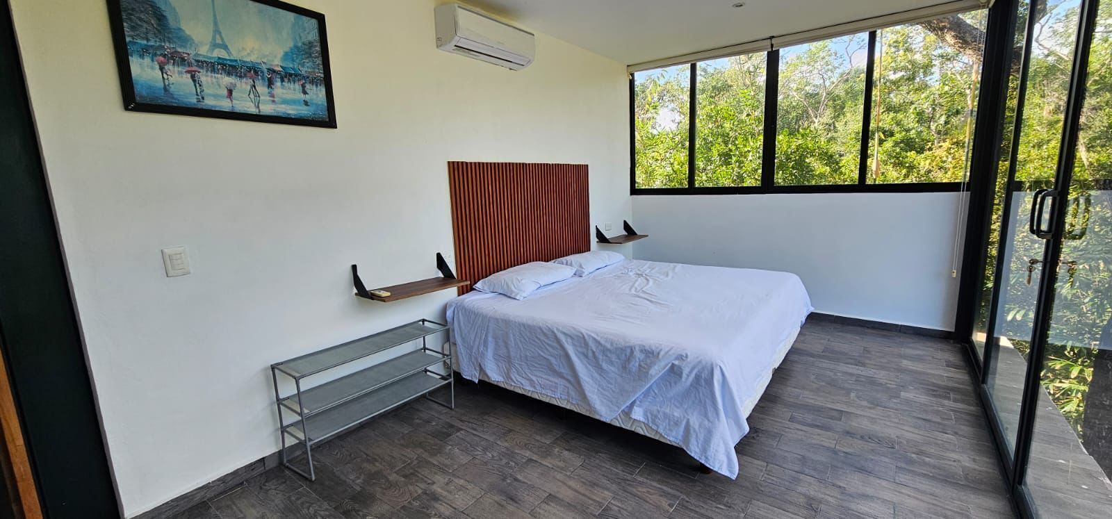 A bedroom with a bed, a window, a painting, and a radiator.