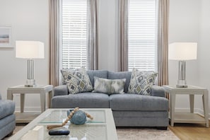 A living room with a grey sofa, two side tables with lamps, a glass coffee table, and a decorative vase.