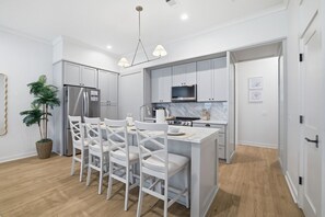 A modern kitchen with white cabinetry, a central island, and a dining area with white chairs.