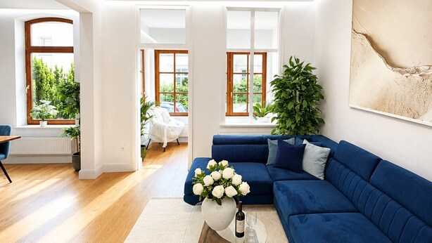 Una sala de estar moderna con un sofá azul, una mesa de centro de vidrio con un jarrón de flores y un cuadro abstracto grande en la pared.