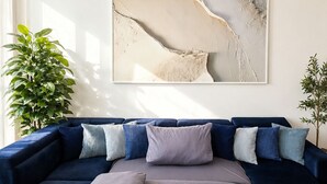 Un sofá modular con una manta y almohadas, un cuadro abstracto grande en la pared y dos plantas en macetas.