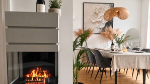 Un interior moderno con chimenea, mesa de comedor, sillas y una lámpara colgante.