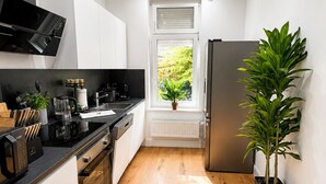 Una cocina moderna con gabinetes blancos, encimera negra, microondas integrado, cafetera y una planta en maceta.