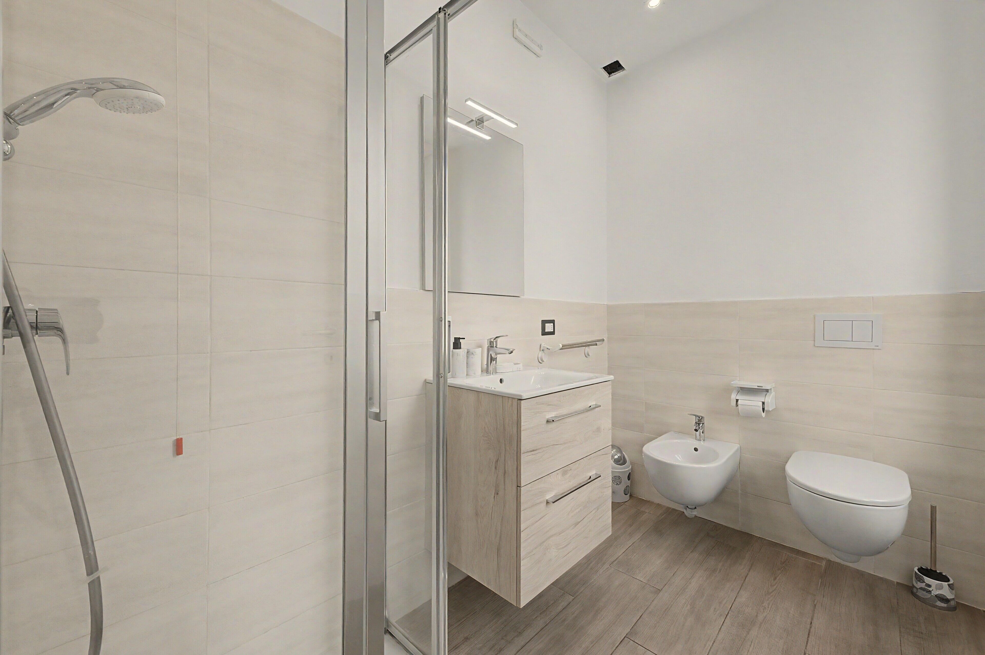 Un bagno moderno con cabina doccia in vetro, lavabo con specchio e water.