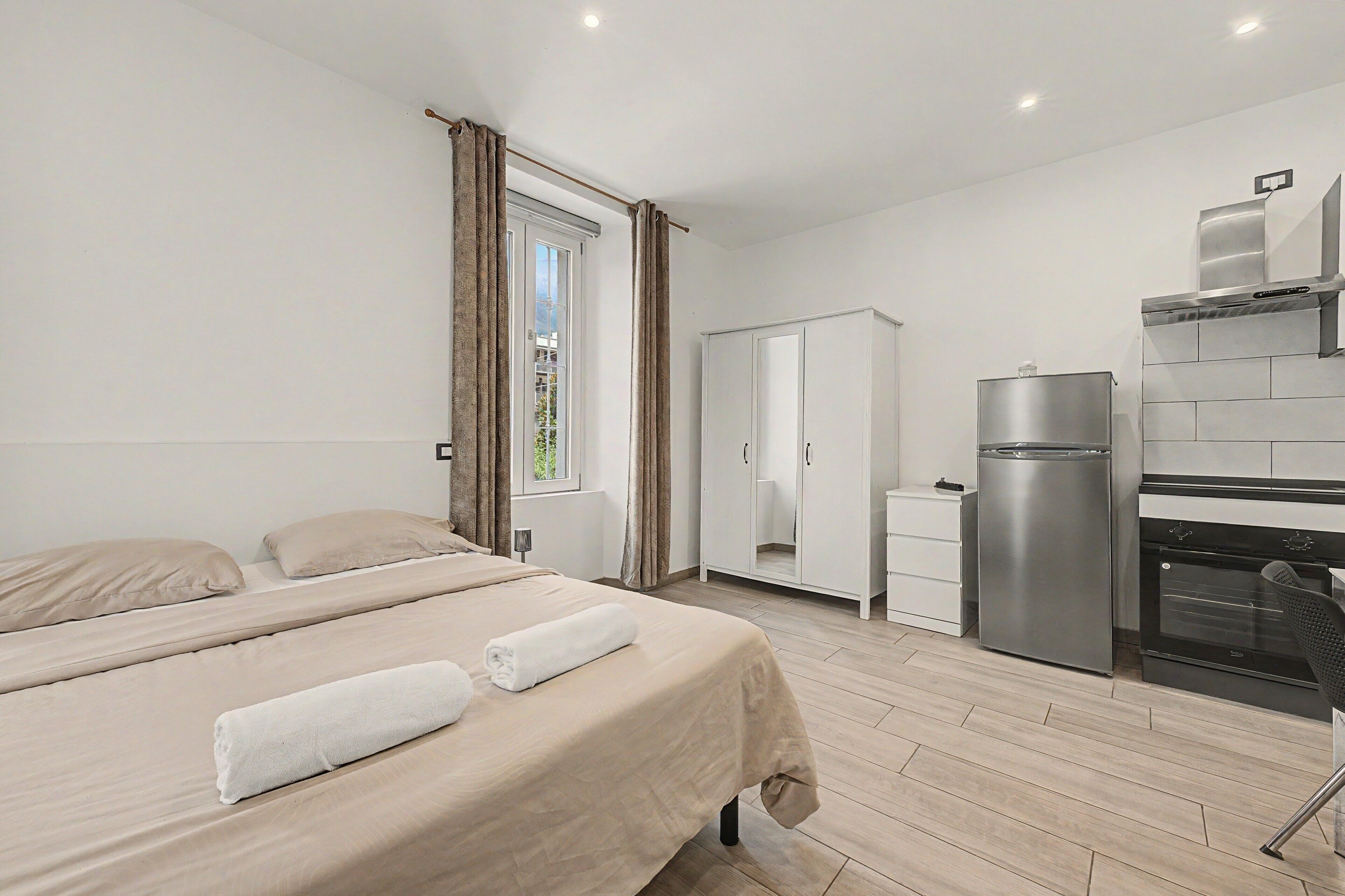 Ein Hotelzimmer mit einem Bett, einem Kleiderschrank, einer Küchenzeile und einem Fenster mit Vorhängen.