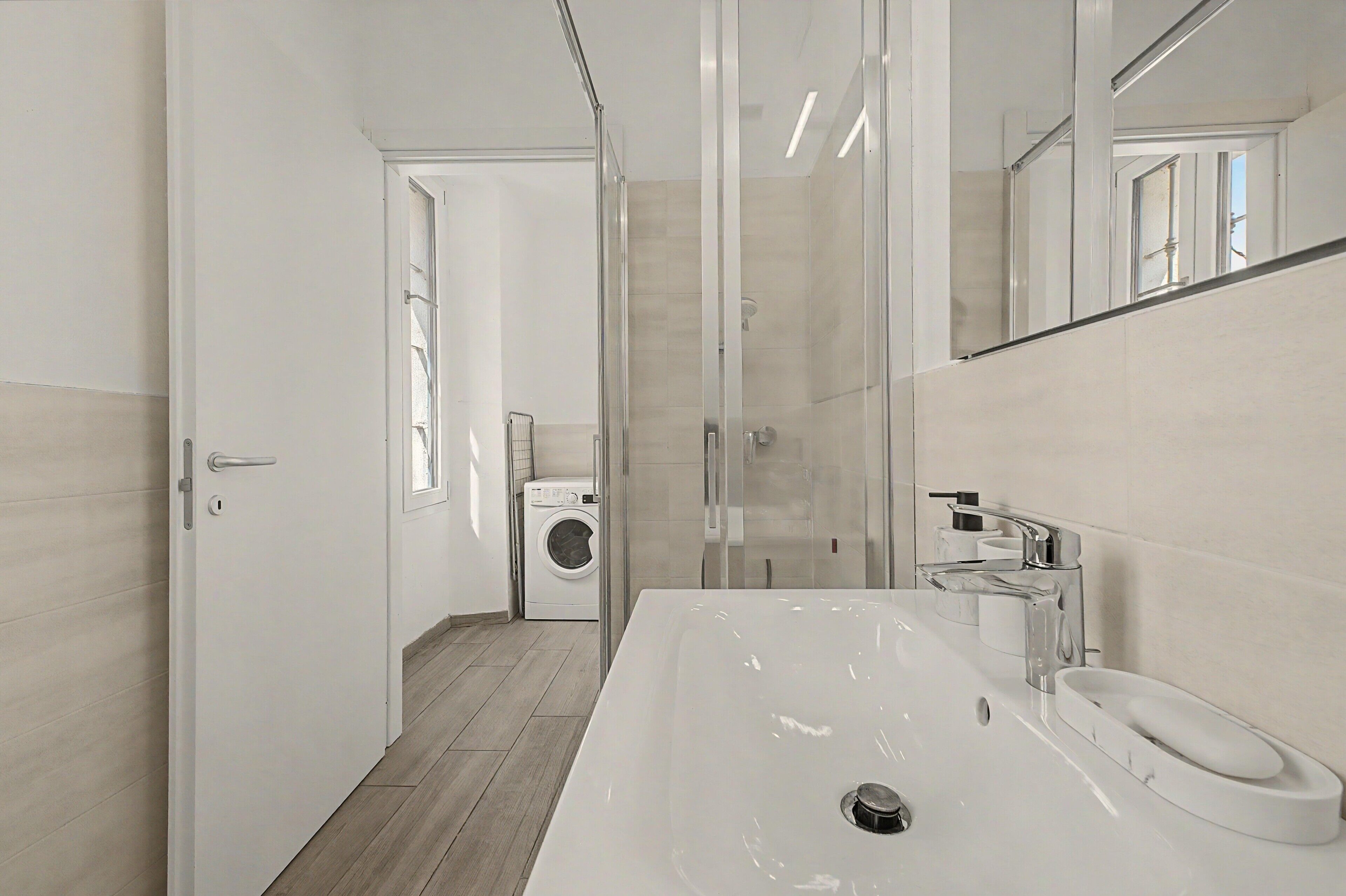 Un bagno moderno con un lavandino grande, uno specchio e una lavatrice sullo sfondo.