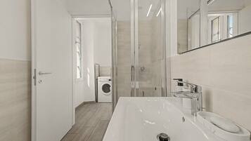 Un bagno moderno con un lavandino grande, uno specchio e una lavatrice sullo sfondo.
