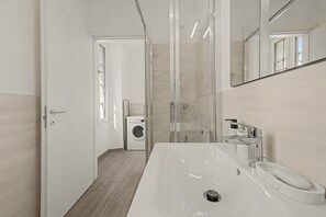Un bagno moderno con un lavandino grande, uno specchio e una lavatrice sullo sfondo.