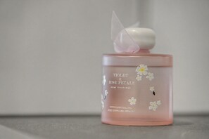 Una bottiglia rosa con tappo bianco, etichettata 'VIOLET & ROSE PETALS HOME FRAGRANCE', contiene un diffusore a stoppino per oli essenziali da 280ml.