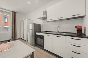 Una cucina moderna con mobili bianchi, un frigorifero in acciaio inox, forno integrato, macchina del caffè e una finestra con tende.