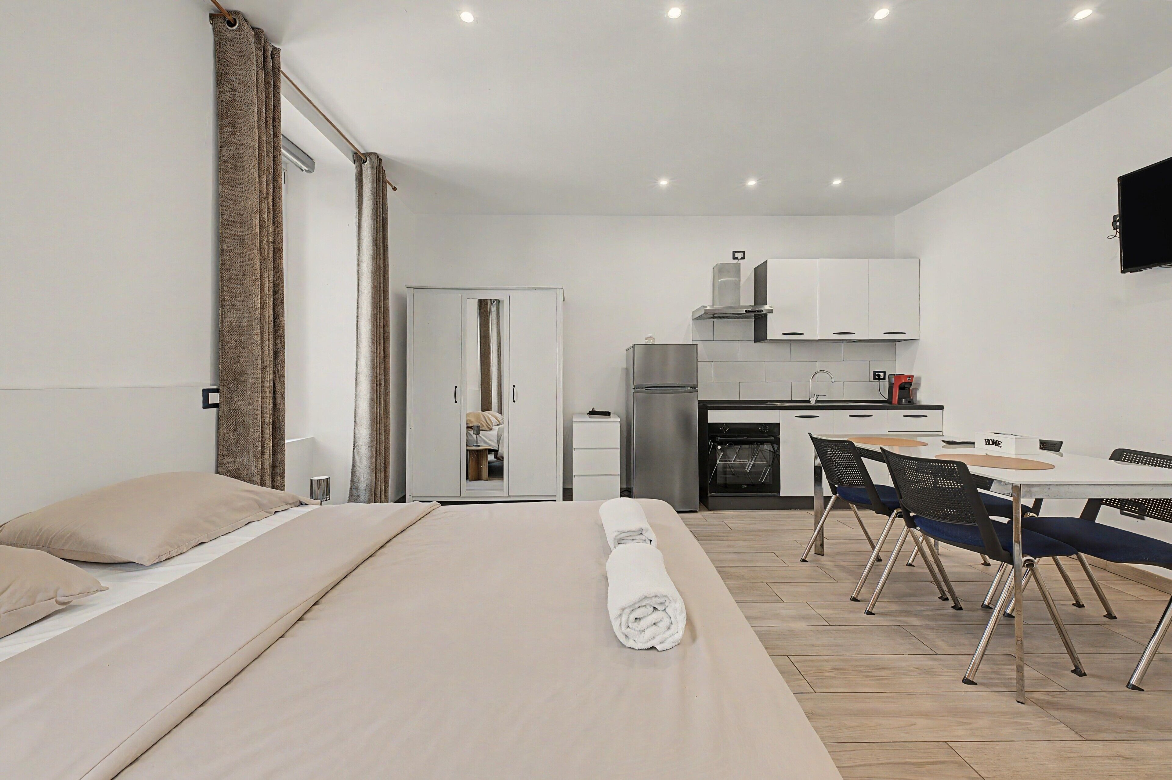 Een moderne slaapkamer met een bed, een keurig opgemaakt bed, een badkamer met douche en een kitchenette met een koelkast, oven en kastjes.