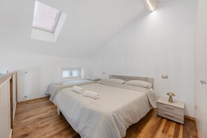 A bedroom with two beds, a skylight, a bedside table with a lamp, and a wooden floor. - Apartment 'Gold' with Wi-Fi and Air Conditioning (Delebio)