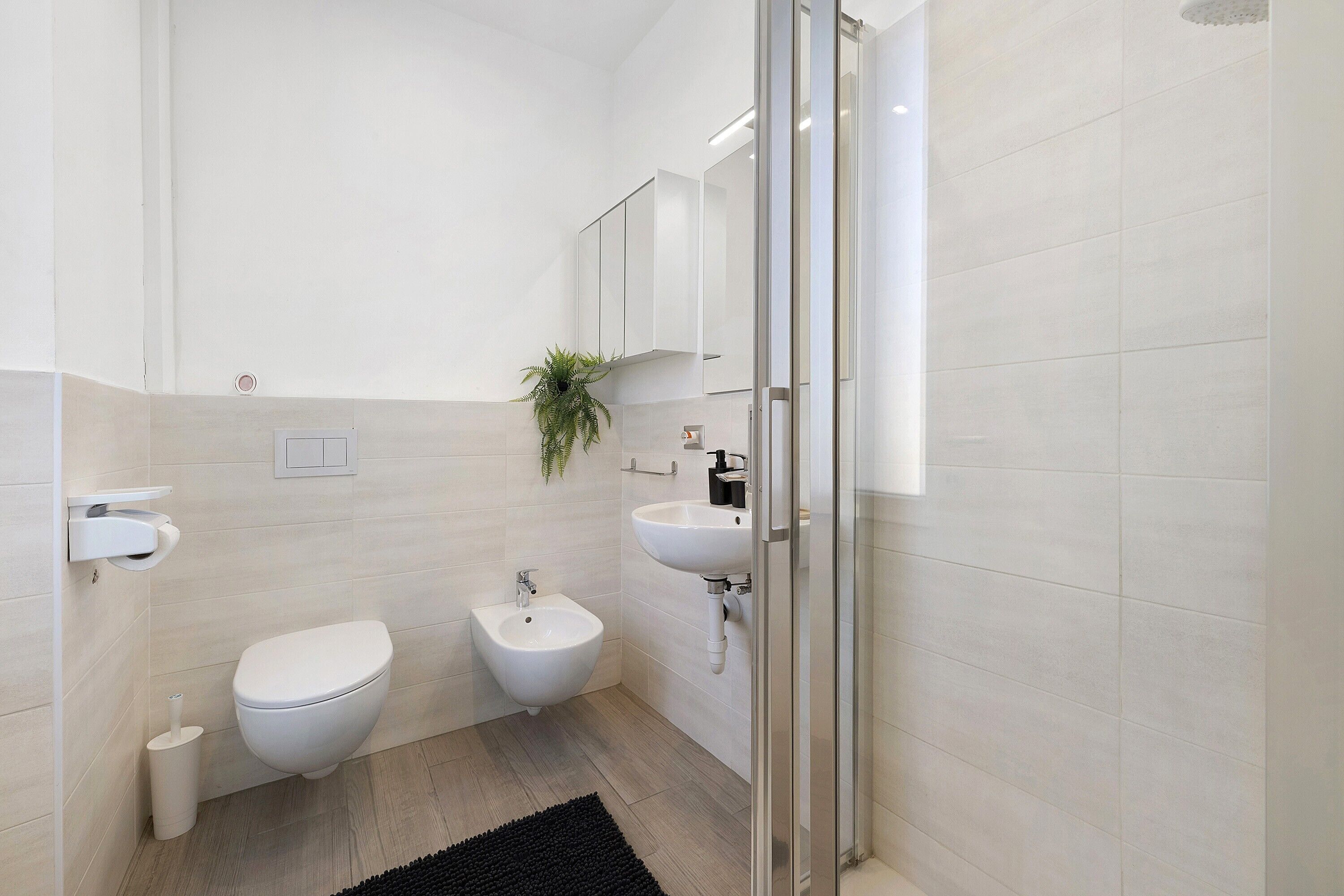 Ein modernes Badezimmer mit Toilette, Bidet, Waschbecken und einer Duschkabine aus Glas.
