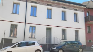 A two-story building with a gated entrance, a white car parked in front, and a dark-colored car parked beside it. - Apartment 'Silver' with Wi-Fi and Air Conditioning (Delebio)