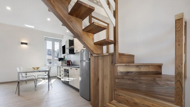 A modern kitchen with a wooden staircase, a dining area with a table and chairs, and a view of the city through a window. - Apartment 'Silver' with Wi-Fi and Air Conditioning (Delebio)