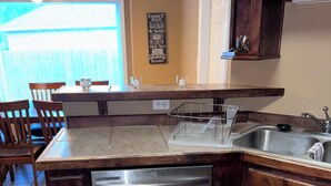 A kitchen with a dishwasher, dark wooden cabinets, a countertop, and a wall-mounted sign. - Creative Heart - Get Away!!   Spacious 4BR/3 Full Bath Home for your Enjoyment. (Gulfport)