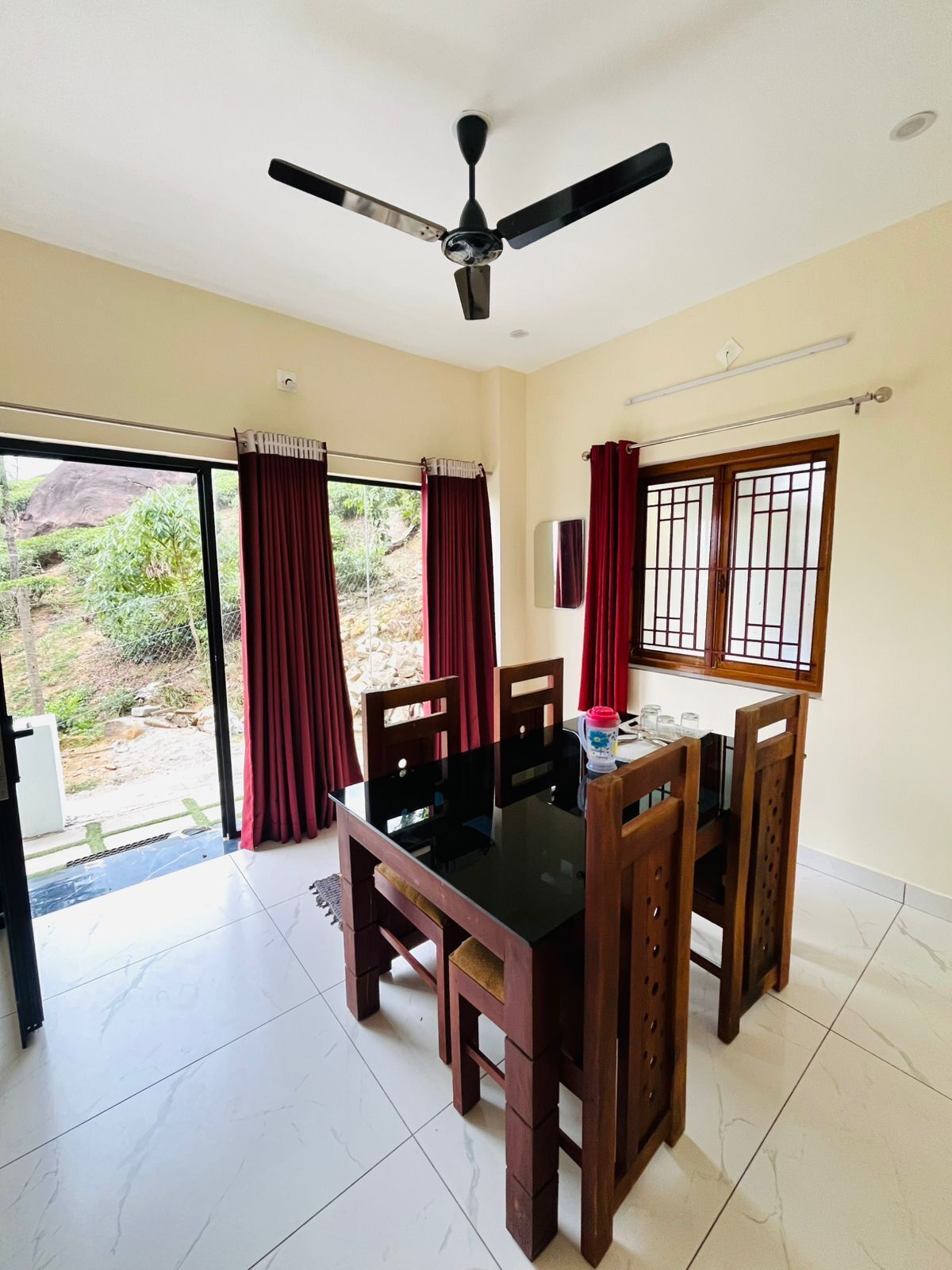 Un comedor con mesa y sillas, un ventilador de techo y vistas a través de un ventanal.