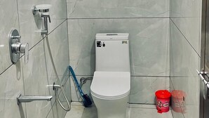 Kylpyhuone, jossa on wc, suihku, pieni ikkuna ja vihreä ämpäri.