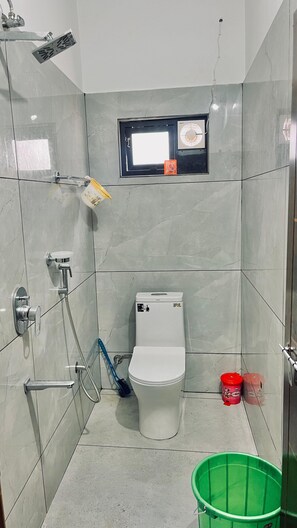 A small bathroom with a toilet, a shower, and a window with a fan.