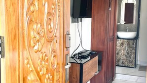 Auki olevat, koristeellisesti kaiverretut puiset ovet, seinälle asennettu litteä televisio, sisäänrakennettu pesuallas ja marmorilaatoitettu lattia.