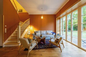 A living room with a staircase, a sofa, two chairs, a coffee table, and large windows. - Sustainable house by forest path near Laer (Meschede)