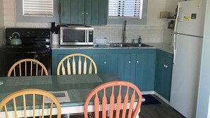 Cozinha compacta com armários verde-água, micro-ondas, fogão e frigorífico. Há duas cadeiras de madeira e uma mesa com um jogo americano.