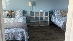 Quarto com duas camas, uma mesa de cabeceira, uma luminária e um estante branco.