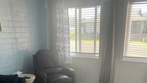 Um quarto com um sofá azul, uma poltrona de couro, uma cesta de vime e uma janela com persianas.