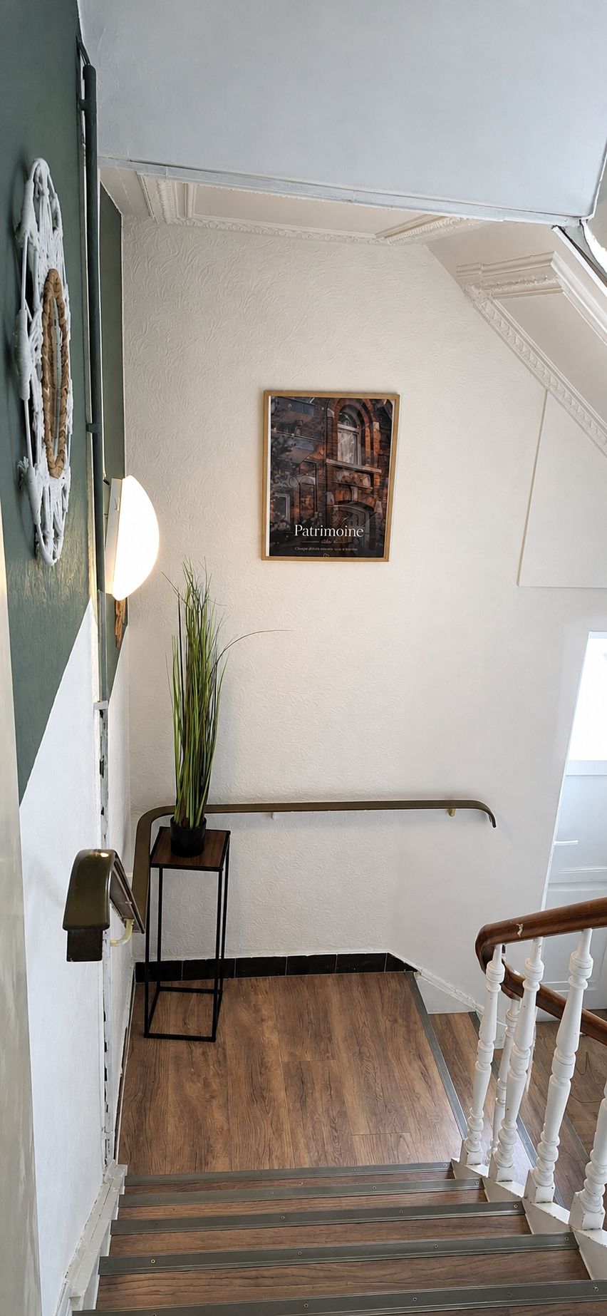 Een trap met houten treden en witte balustrades, die uitkomt op een plateau met een lijst en een potplant.