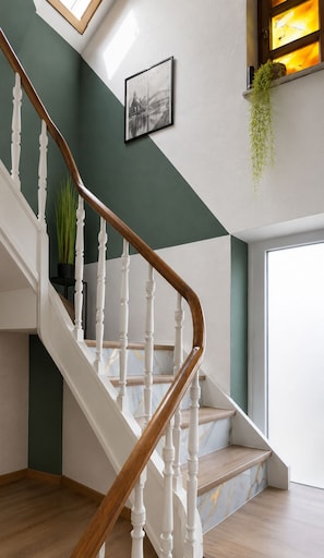 A staircase with white balusters and wooden handrails, leading to a landing with a framed picture and a hanging plant.