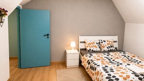 A bedroom with a teal door, a bedside table with a lamp, a bed with patterned bedding, and a small rug.