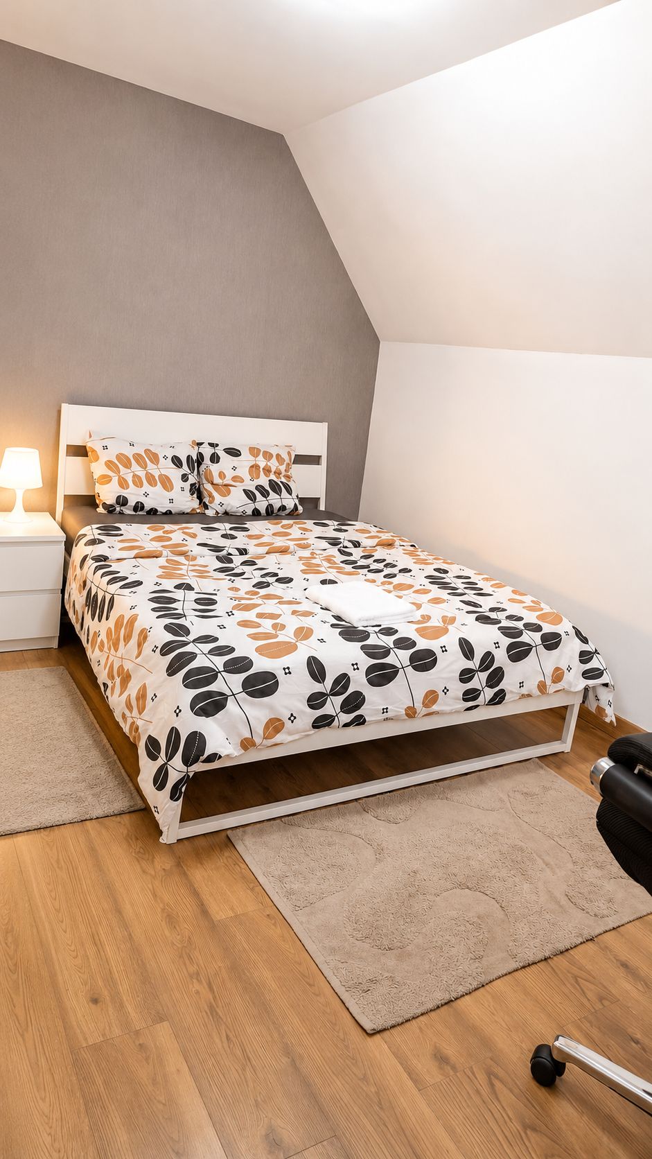 Een slaapkamer met een bed, nachtkastje, lamp, bureau en stoel.