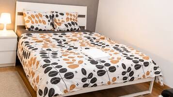 Een slaapkamer met een bed, nachtkastje, lamp, bureau en stoel.