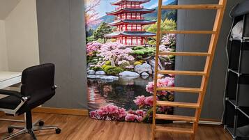 Una habitación con un escritorio, una silla de oficina negra, una escalera de madera y una pared con un mural panorámico de una pagoda y flores de cerezo.