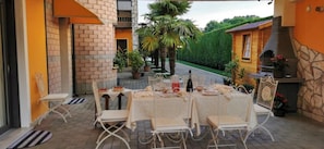 Une terrasse extérieure avec une table dressée pour le repas, entourée de chaises, et une cheminée en pierre.