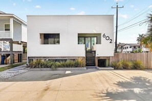 A modern two-story house with a white exterior, a front door, and a number '602' on the side. - Resting Beach Face | Private Pool • Modern Coastal Retreat • Prime 11th St Location (Port Aransas)