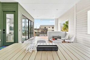 A balcony with a wooden table, white chairs, a grill, and a view of neighboring buildings. - Resting Beach Face | Private Pool • Modern Coastal Retreat • Prime 11th St Location (Port Aransas)