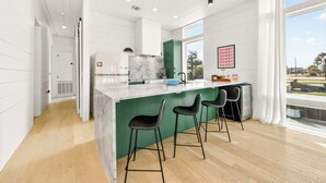 A modern kitchen with a marble countertop, green accent wall, and bar stools. - Resting Beach Face | Private Pool • Modern Coastal Retreat • Prime 11th St Location (Port Aransas)