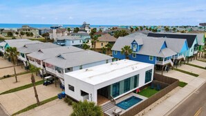 A modern house with a large glass window, a swimming pool, and a view of the ocean. - Resting Beach Face | Private Pool • Modern Coastal Retreat • Prime 11th St Location (Port Aransas)