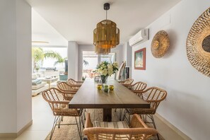 A dining area with a long wooden table, wicker chairs, and a hanging light fixture.