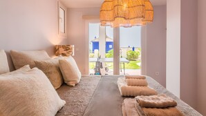 A bedroom with a large bed, a hanging light fixture, and a view of a blue building through a window. - Villa 'Los Altos' with Sea Views, Wi-Fi, and Air Conditioning (Almuñécar)