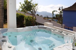 Un jacuzzi con vista a las montañas, una piscina y un edificio azul.