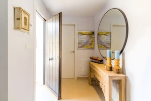 Un couloir avec une armoire en bois, une porte, une console sur laquelle sont posées des bougies et un tableau accroché au mur.