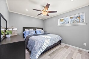 A bedroom with a bed, a ceiling fan, a window with blinds, a mirror, and a dresser. - Charming Two-Story Apartment in Irving (Irving)