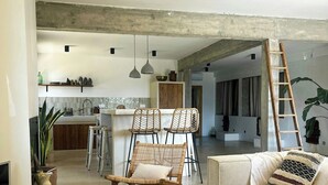 Un vaste espace de vie comprenant une table basse en bois, des fauteuils en osier, un canapé et, au fond, une cuisine.
