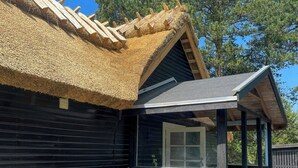 Uma cabana de madeira com telhado de palha, varanda coberta e uma janela.
