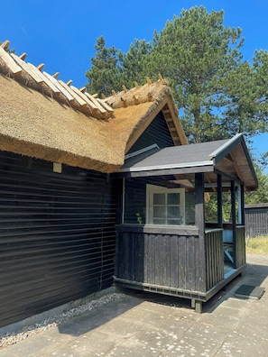 Eine Holzhütte mit Strohdach und überdachter Veranda sowie einem Fenster.