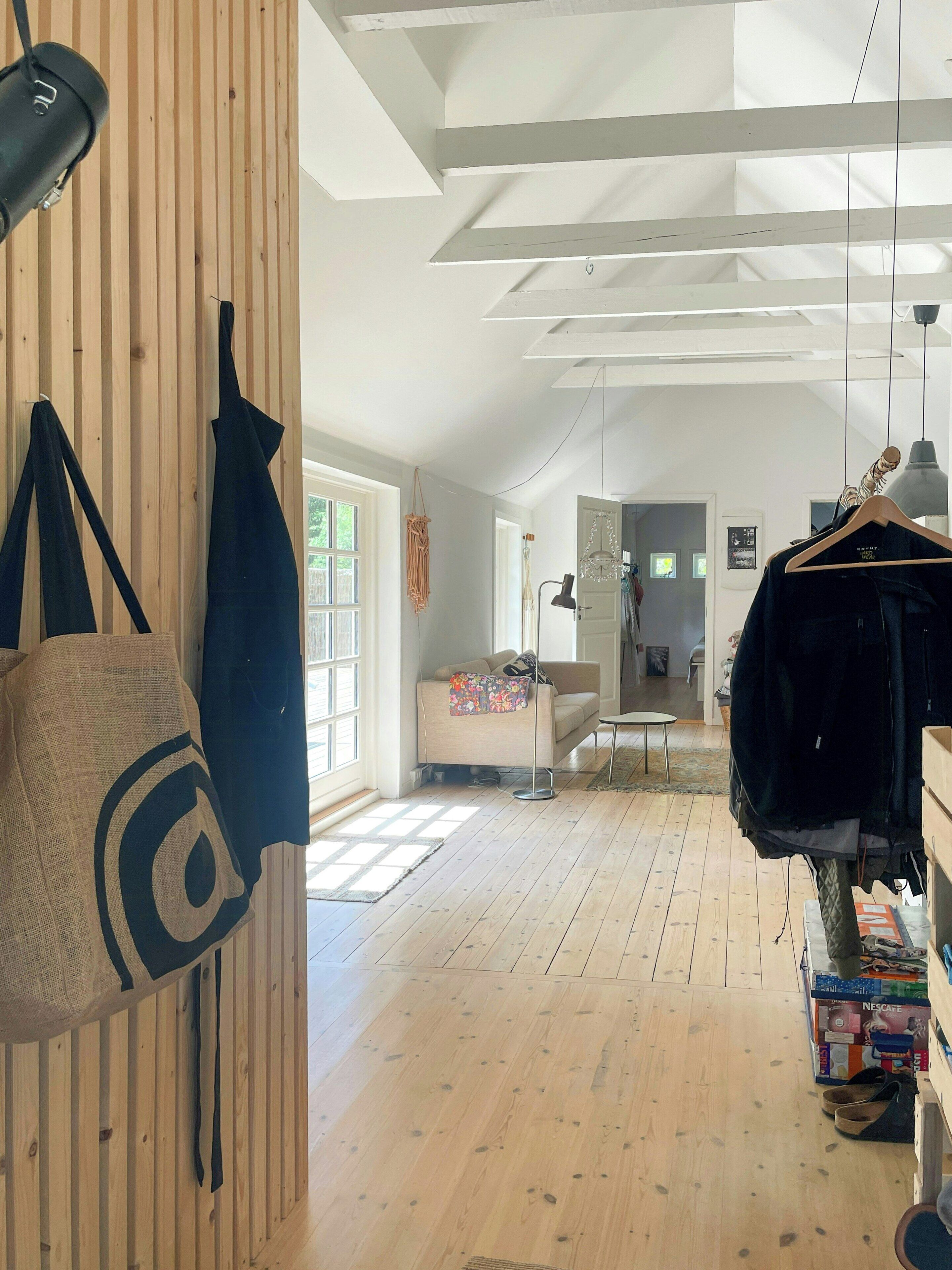 Une pièce spacieuse avec un plancher en bois, un canapé, un porte-manteau mural et une machine à café Nescafé.